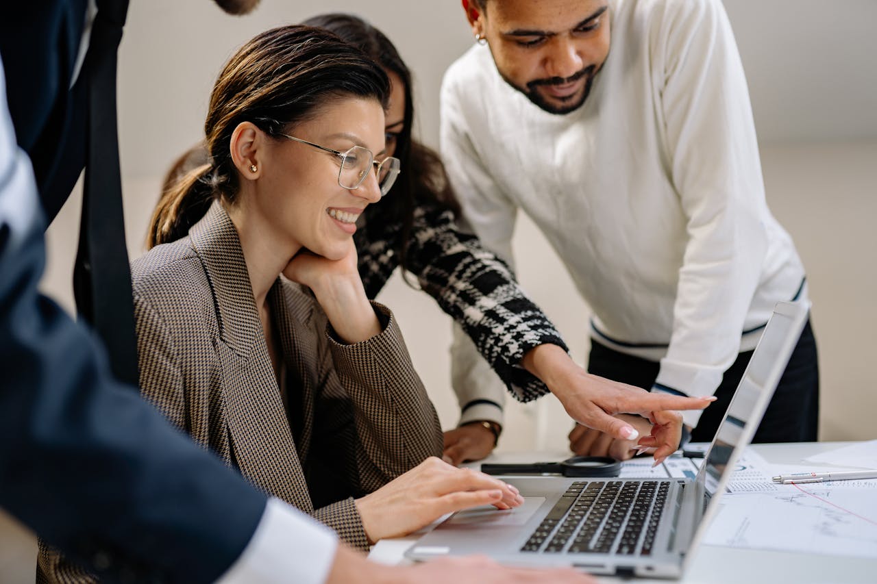 Diverse group of adults working together on a laptop in an office setting.