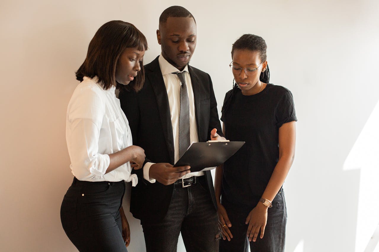 A team of professionals discussing work around a clipboard in an office setting.