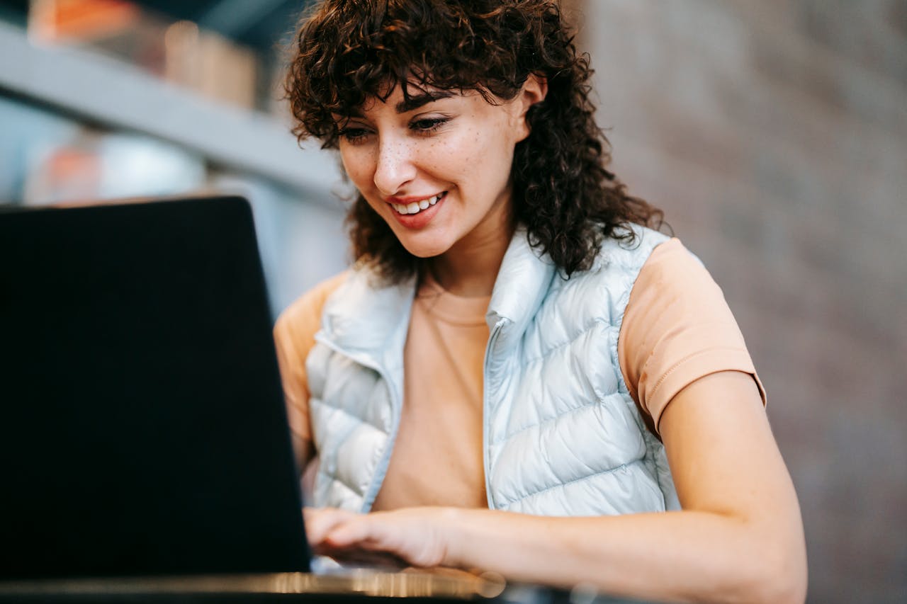 Cheerful woman using a laptop in a modern café. Ideal for freelance or remote work themes.
