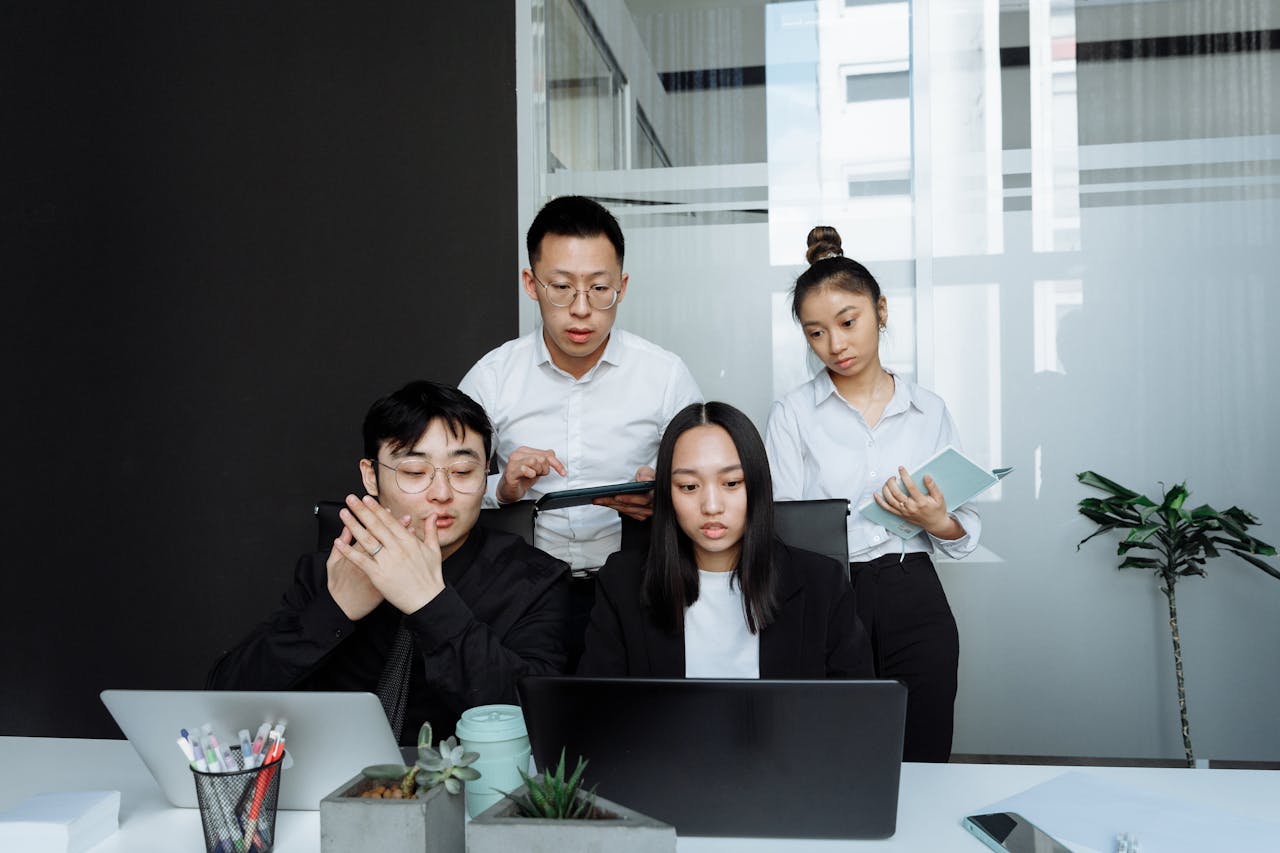 A diverse business team collaborates on projects in a modern office setting, using technology and notes.